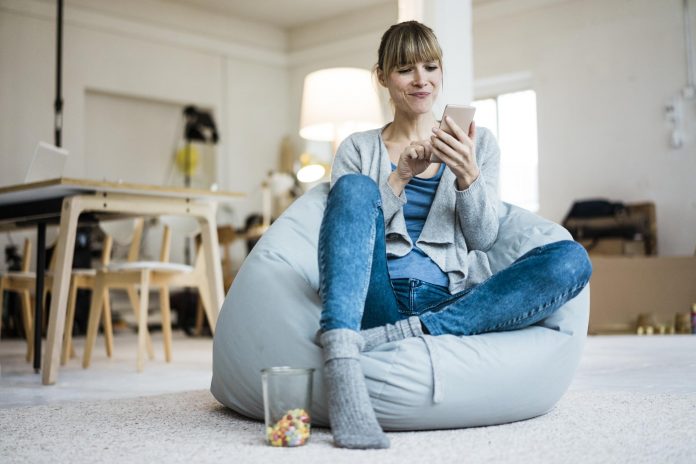 Smiling woman sitting in beanbag using cell phone Telco e Media: necessari investimenti in infrastrutture