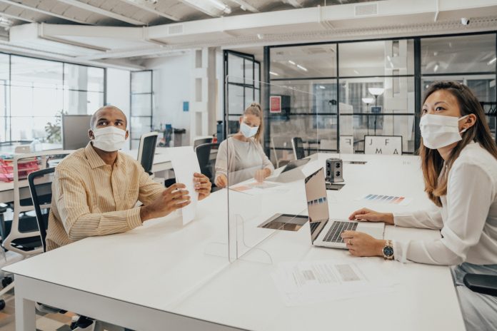 Businesspeople working at office with glass partition dividing them Tecnologia inadeguata, dipendenti demotivati