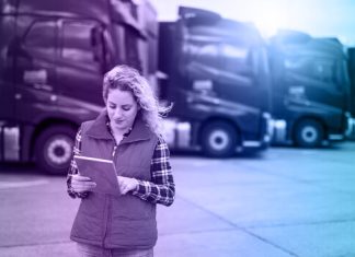 Truck driver holding tablet and checking route for new destination. In background parked truck vehicles. Transportation service.