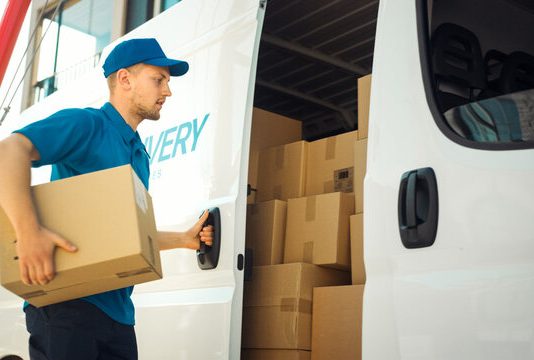 Courier Takes out Cardboard Box Package from Openned Delivery Van and Closes the Door. Delivering Postal Parcel to Customer.